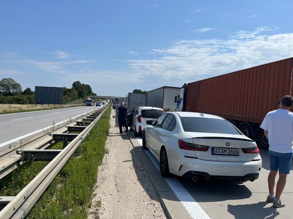 Traffic queue on the E40 motorway near Jarostów, Poland, with cars and lorries lined up on the carriageway and motorists standing beside their vehicles during a lengthy delay on a sunny day.