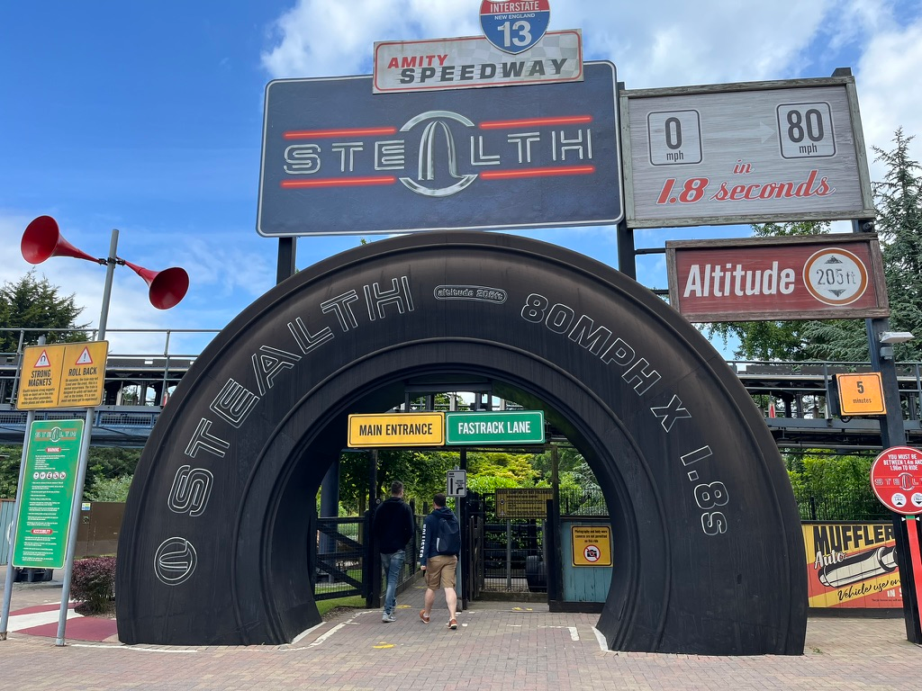 Entrance to Stealth roller coaster at Thorpe Park, featuring a giant tyre-shaped archway and signage highlighting the ride's launch from 0 to 80 mph in 1.8 seconds and a height of 205 feet.