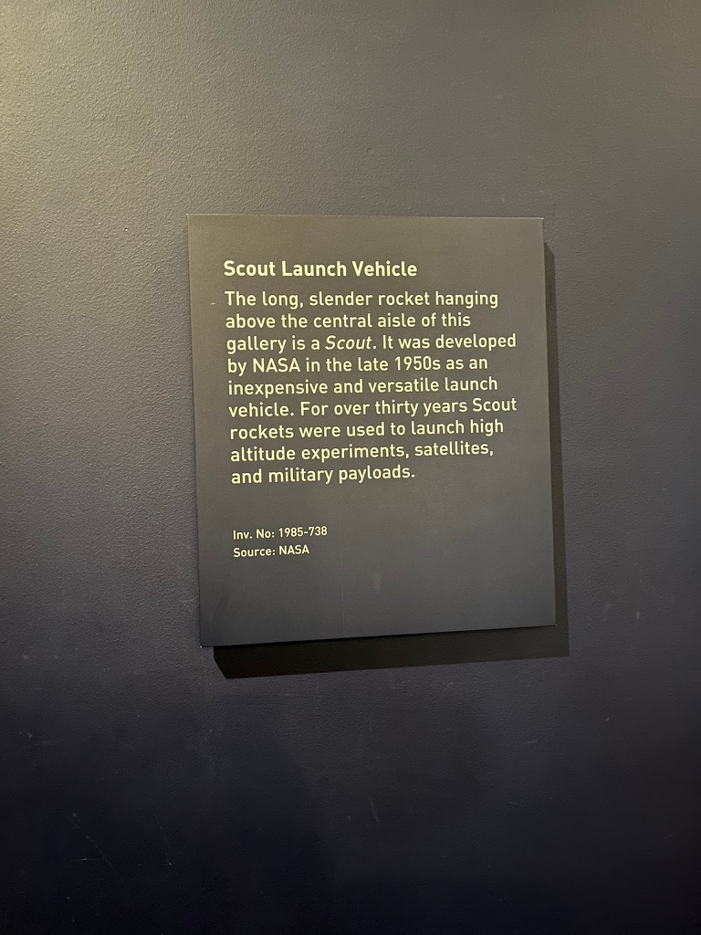 Museum information panel titled "Scout Launch Vehicle", explaining the history of NASA's Scout rocket programme and its use for launching scientific experiments, satellites and military payloads, mounted on a dark gallery wall.