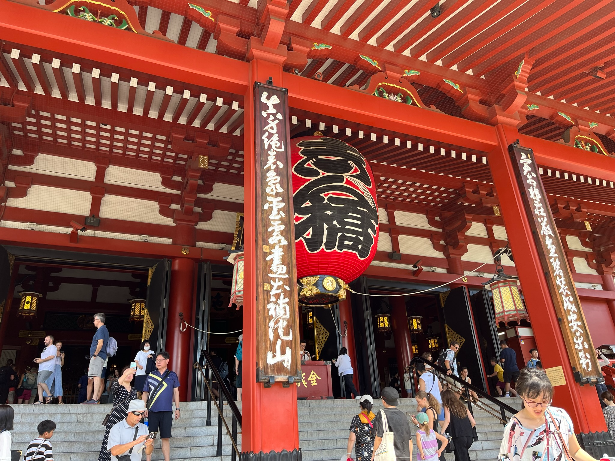 Visitors gather beneath the giant red Kaminarimon lantern at Sensō-ji Temple, surrounded by ornate vermilion columns and traditional architectural details in Asakusa.
