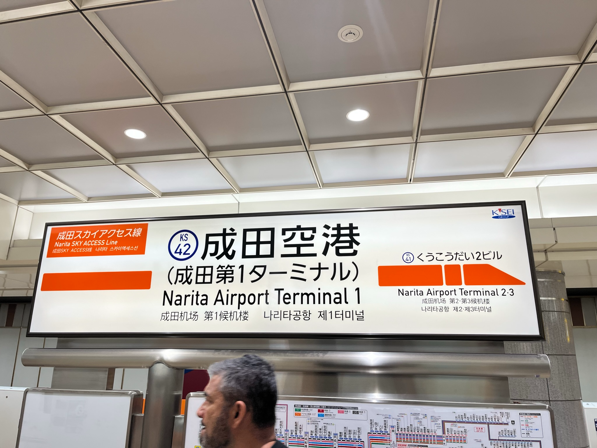 Station sign for Narita Airport Terminal 1 on the Narita Sky Access Line, displaying Japanese, English, Chinese and Korean text inside the airport rail station.