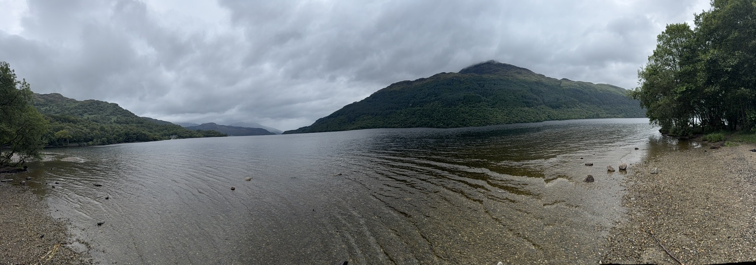 Panoramic view across Loch Lomond beneath dark storm clouds.
