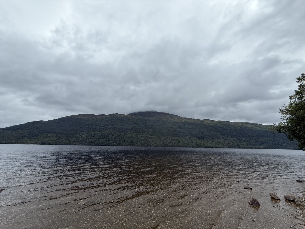 Loch Lomond viewed from the shoreline beneath low cloud and dark skies.