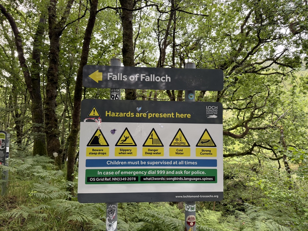 Falls of Falloch footpath sign and safety notice in woodland.