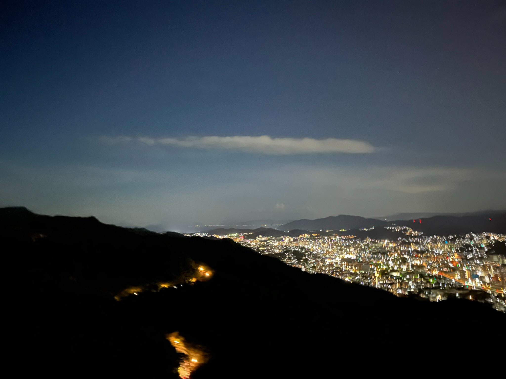 Night view from Mount Inasa overlooking Nagasaki, with city lights stretching across hillsides and valleys beneath a dark sky, creating a dramatic urban panorama after sunset.