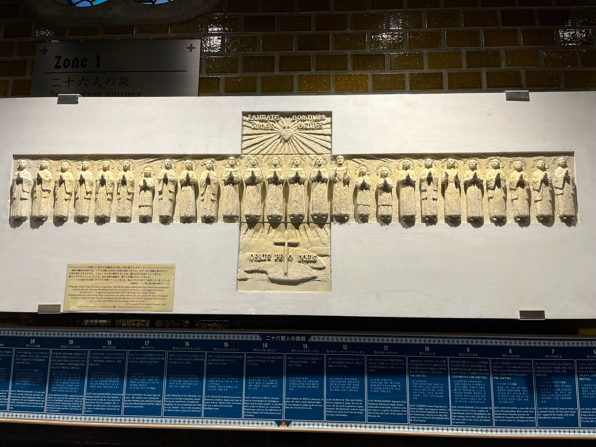Relief sculpture depicting the Twenty-Six Martyrs displayed inside a museum in Nagasaki, with historical information panels and exhibit signage explaining their story and journey.