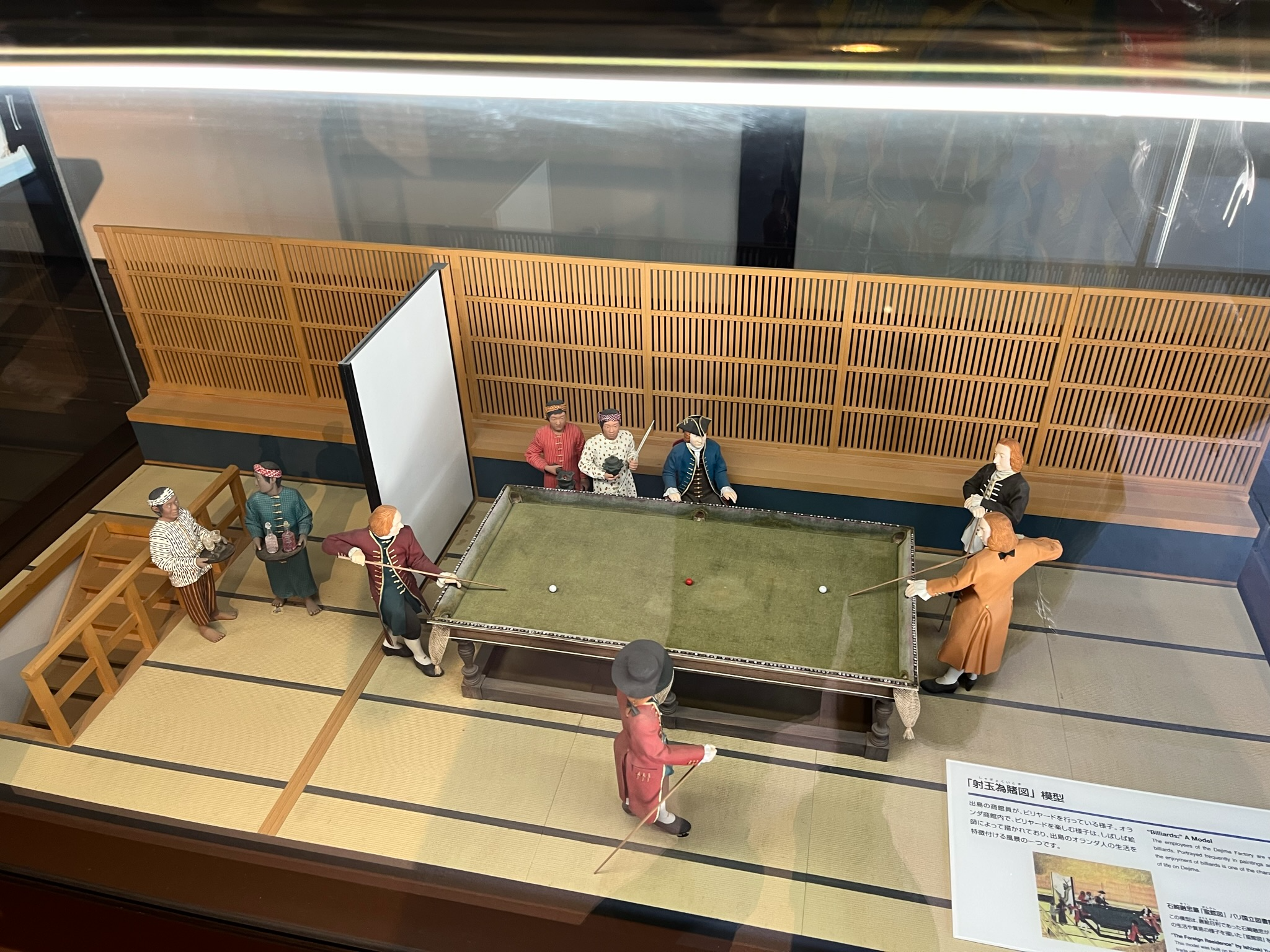 Museum diorama at Dejima in Nagasaki showing Dutch merchants and Japanese attendants gathered around a billiards table inside a reconstructed Edo-period trading post.