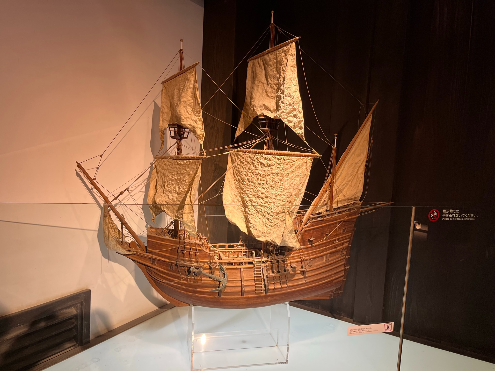 Scale model of a wooden European sailing ship displayed at Dejima in Nagasaki, featuring detailed rigging, masts, sails and deck structures inside a museum exhibit.