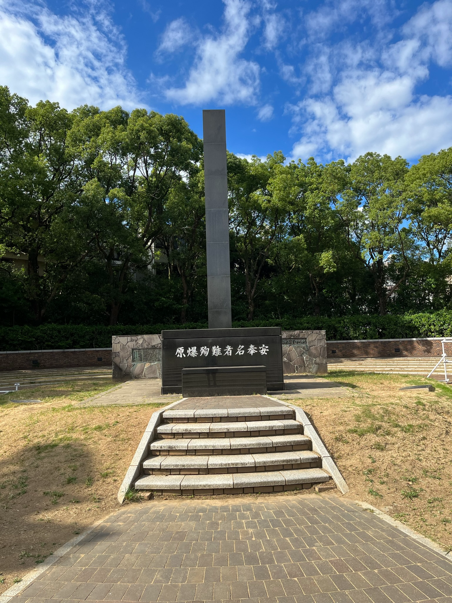 Memorial monument at the Nagasaki National Peace Memorial Hall for the Atomic Bomb Victims, featuring a tall black stone pillar set within landscaped grounds and trees.