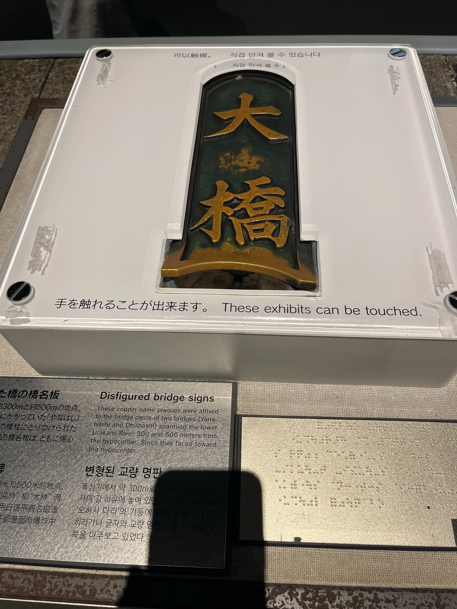 Disfigured copper bridge nameplate displayed at the Nagasaki Atomic Bomb Museum, showing damage caused by the atomic bombing and preserved as a historical artefact.