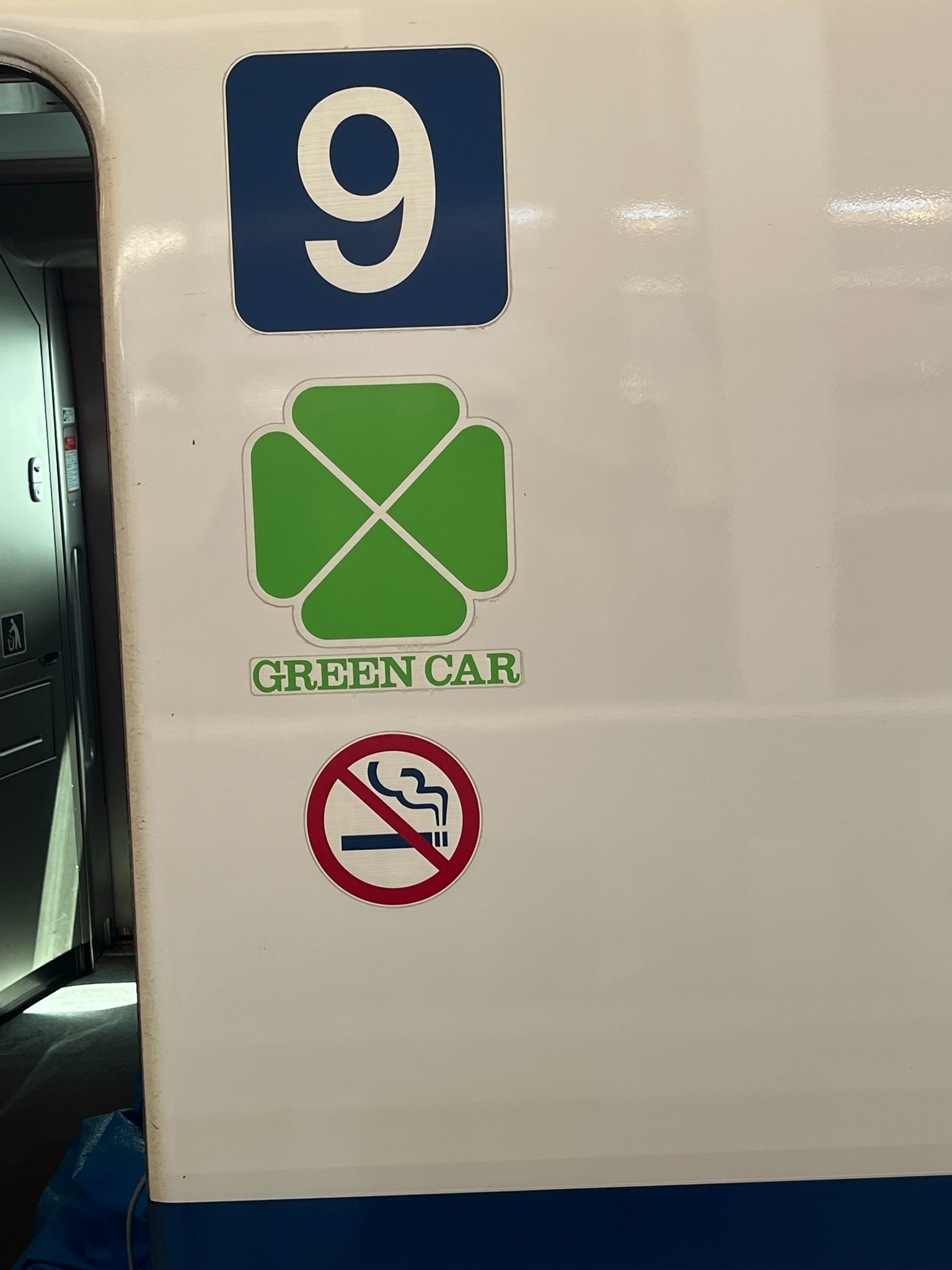 Green Car sign and Car 9 marker on a Shinkansen bullet train, indicating the premium-class carriage entrance alongside a no-smoking symbol.