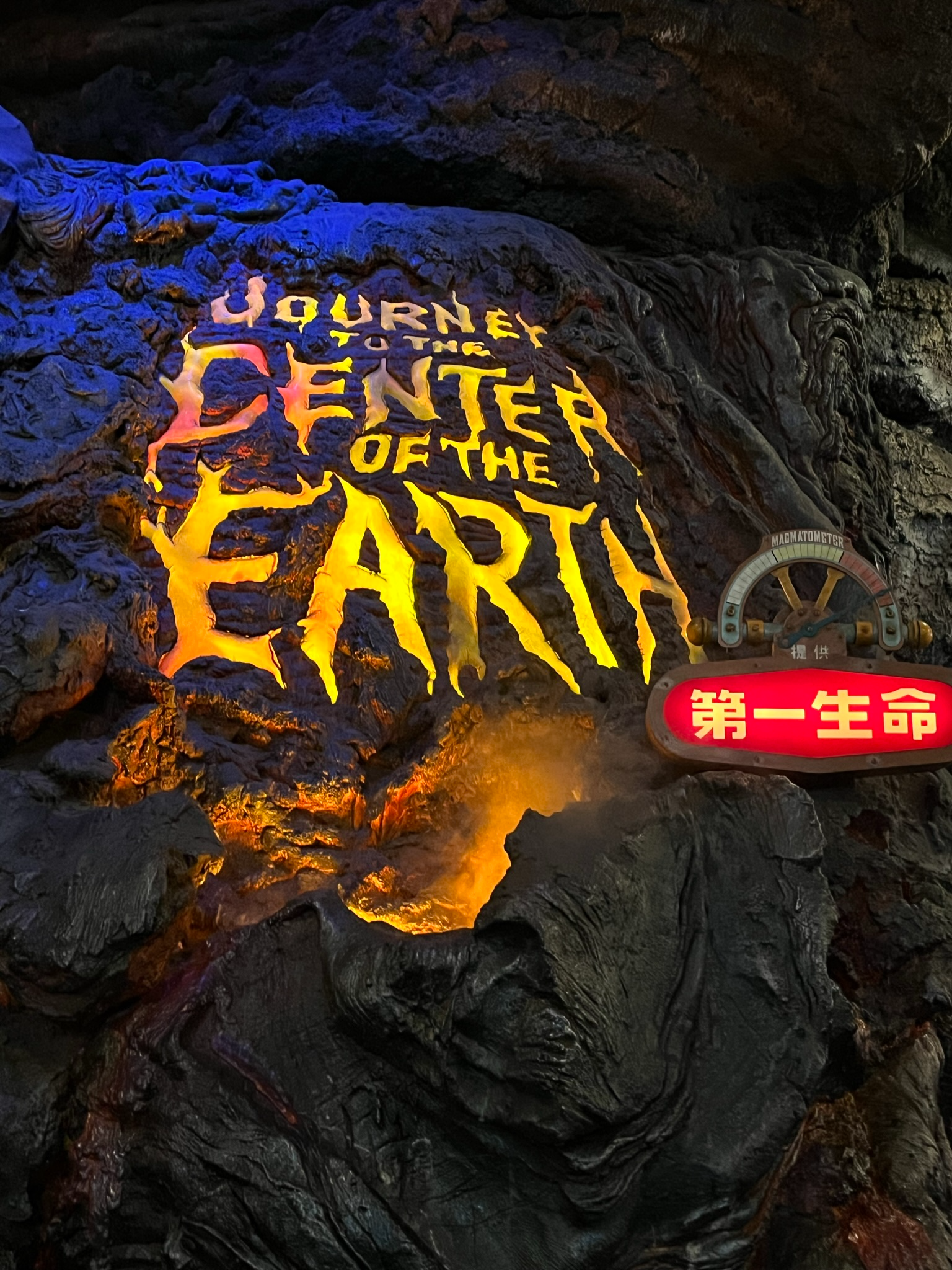 Journey to the Center of the Earth attraction sign at Tokyo DisneySea, featuring glowing lettering carved into volcanic rock beside themed cave walls and magma-inspired lighting.