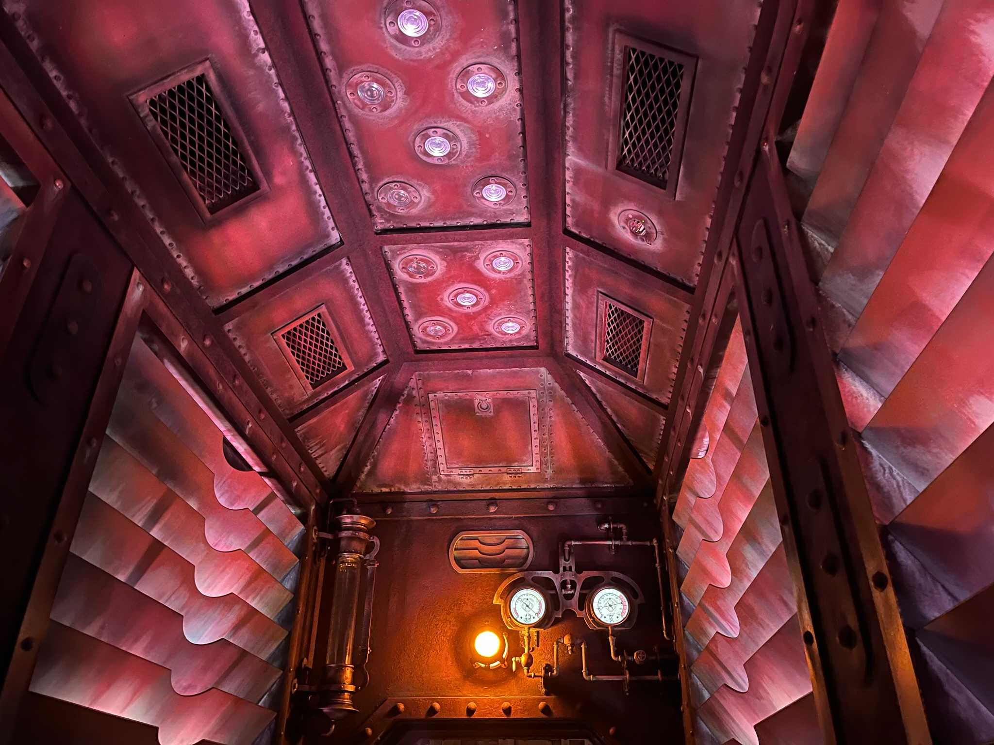Interior of a Journey to the Center of the Earth ride vehicle at Tokyo DisneySea, featuring riveted metal panels, pressure gauges, pipes and warm atmospheric lighting.