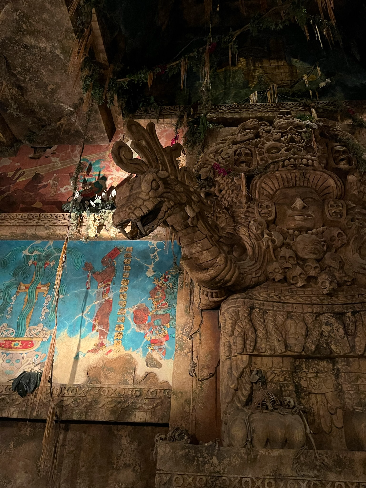 Ancient stone carvings and temple ruins inside Tokyo DisneySea's Temple of the Crystal Skull attraction, featuring weathered sculptures, murals and dramatic atmospheric lighting.