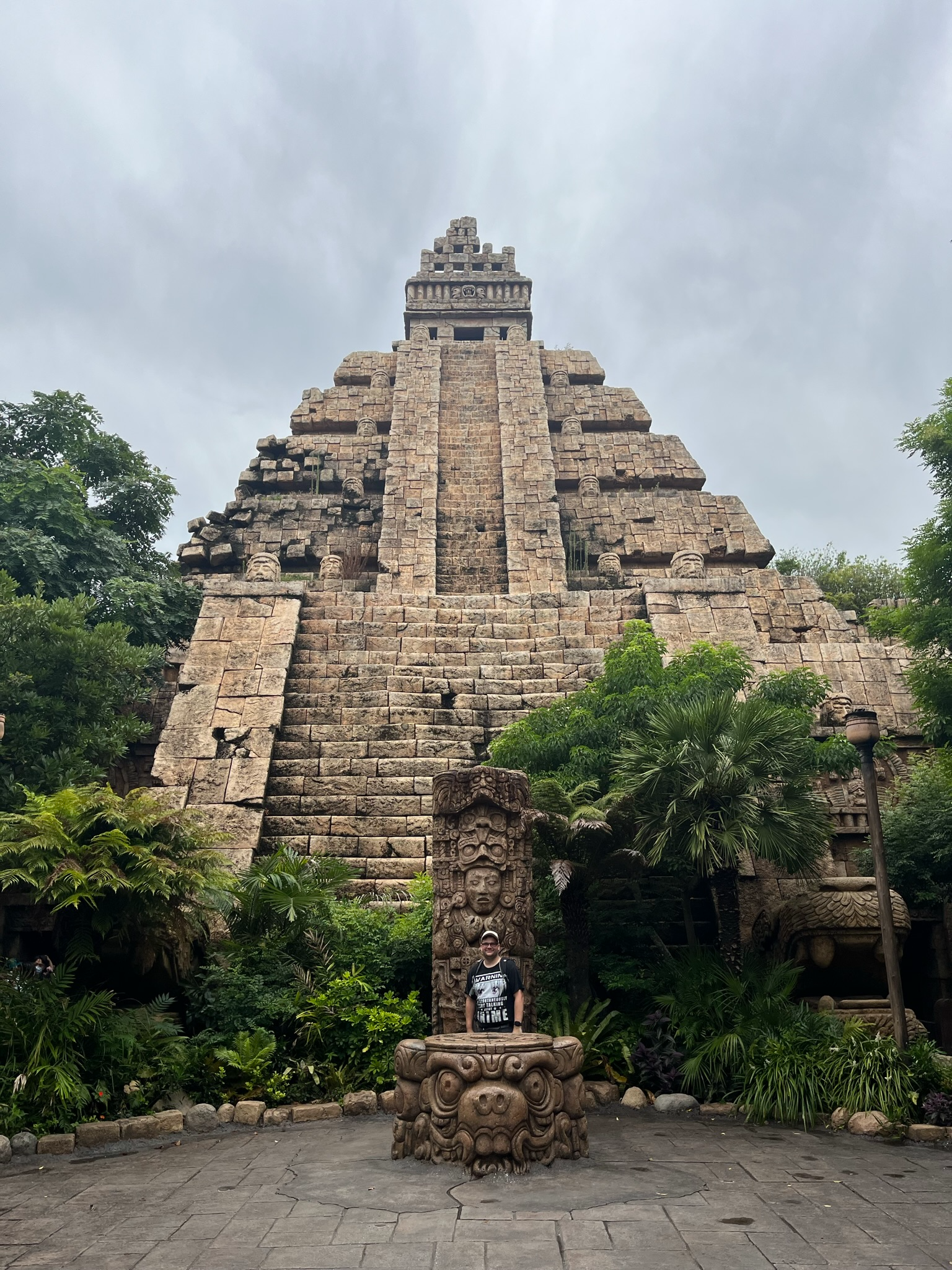 The Temple of the Crystal Skull at Tokyo DisneySea, featuring a towering Mesoamerican-style pyramid surrounded by tropical plants, stone carvings and dramatic storm clouds overhead.