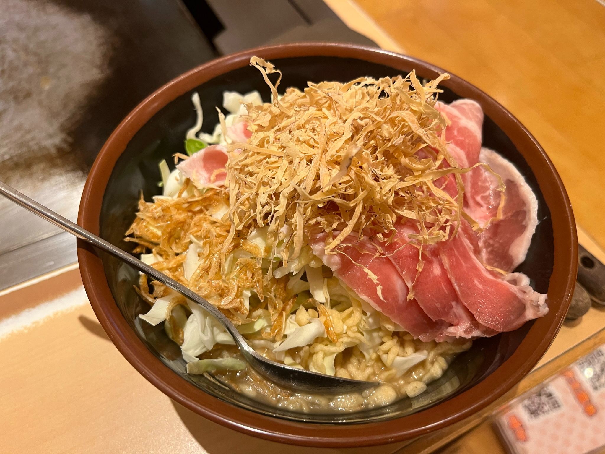 Bowl of monjayaki ingredients including sliced pork, cabbage, tempura flakes and batter, ready to be cooked on a teppan grill at a Japanese restaurant.