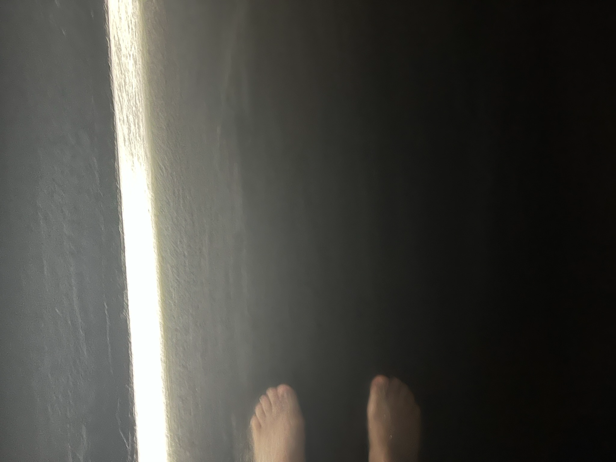 Bare feet standing in shallow water inside a dark TeamLab Planets installation, with a bright strip of light reflected across the surface of the immersive artwork.