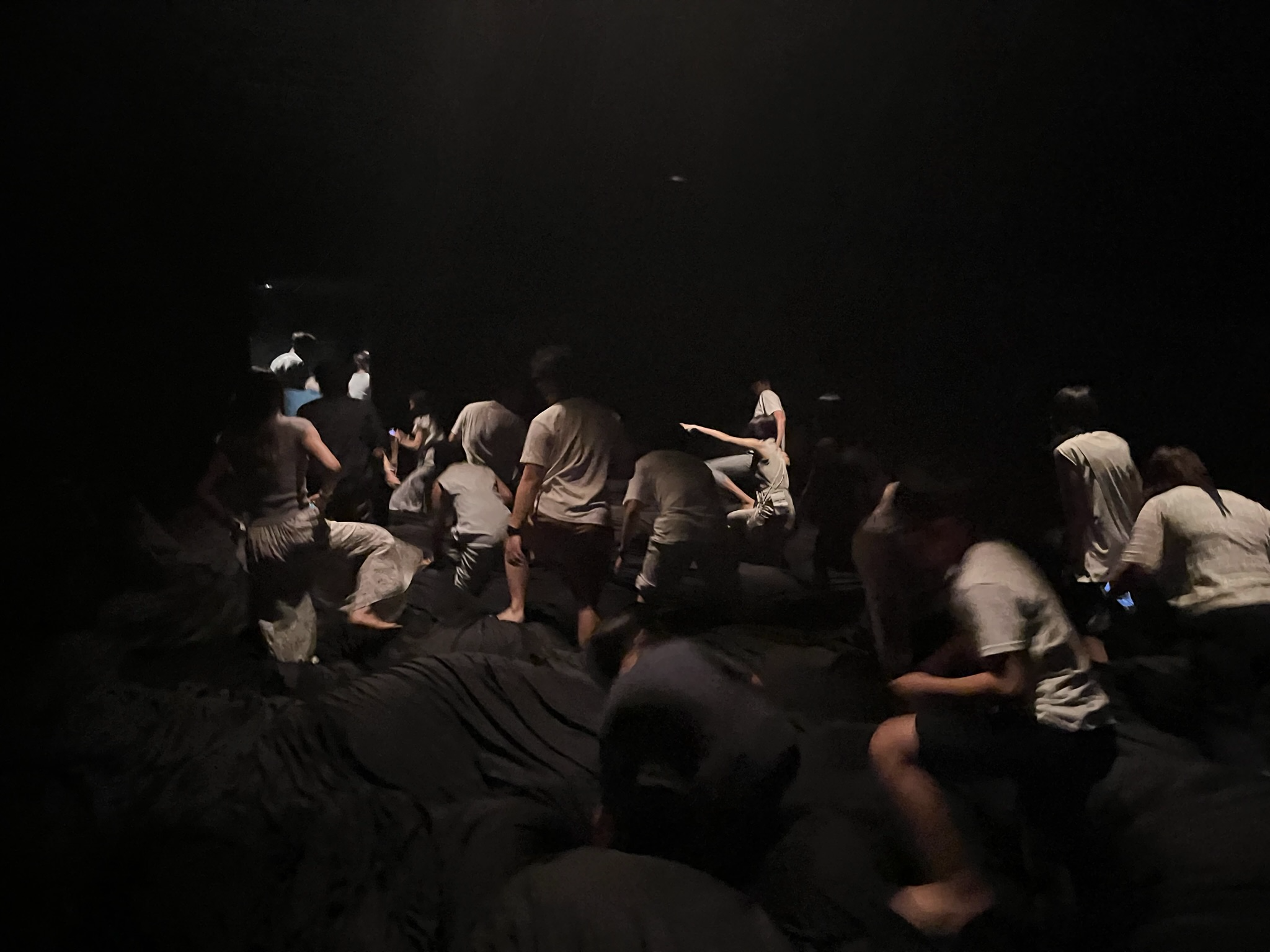 Visitors move through a dark TeamLab Planets installation, climbing across soft uneven surfaces as the immersive artwork responds to movement and interaction.