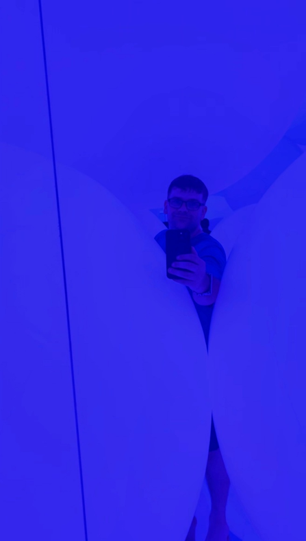 Visitor taking a mirror selfie inside a blue-lit TeamLab Planets installation, surrounded by large soft white forms that create a maze-like immersive environment.
