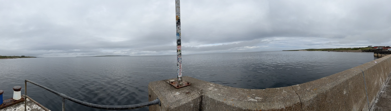 Panoramic view from John O' Groats harbour across calm waters under grey skies.