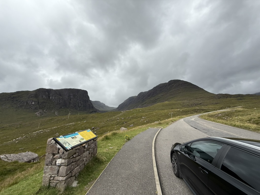 Mountain road viewpoint on the Bealach na Bà with dramatic Highland scenery and a parked car.