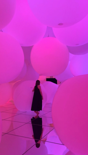 Large glowing pink spheres fill a mirrored room at TeamLab Planets Tokyo, with visitors walking among the illuminated forms as colours change throughout the installation.