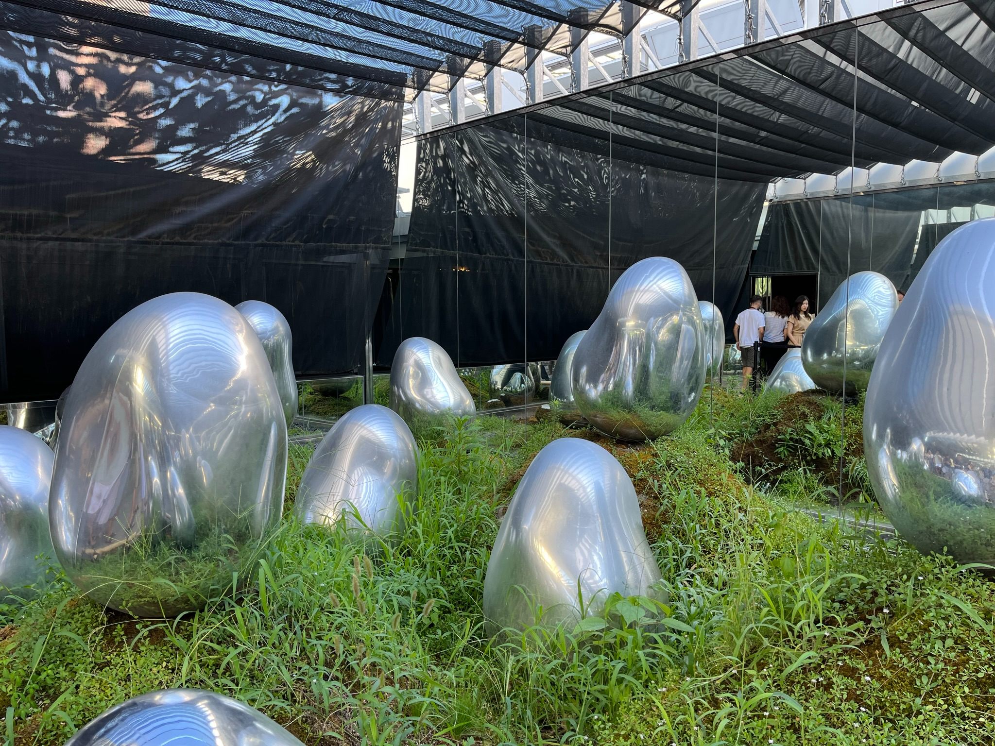 Reflective silver sculptures rise from a moss and grass garden at TeamLab Planets Tokyo, surrounded by mirrored walls that multiply the installation into the distance.