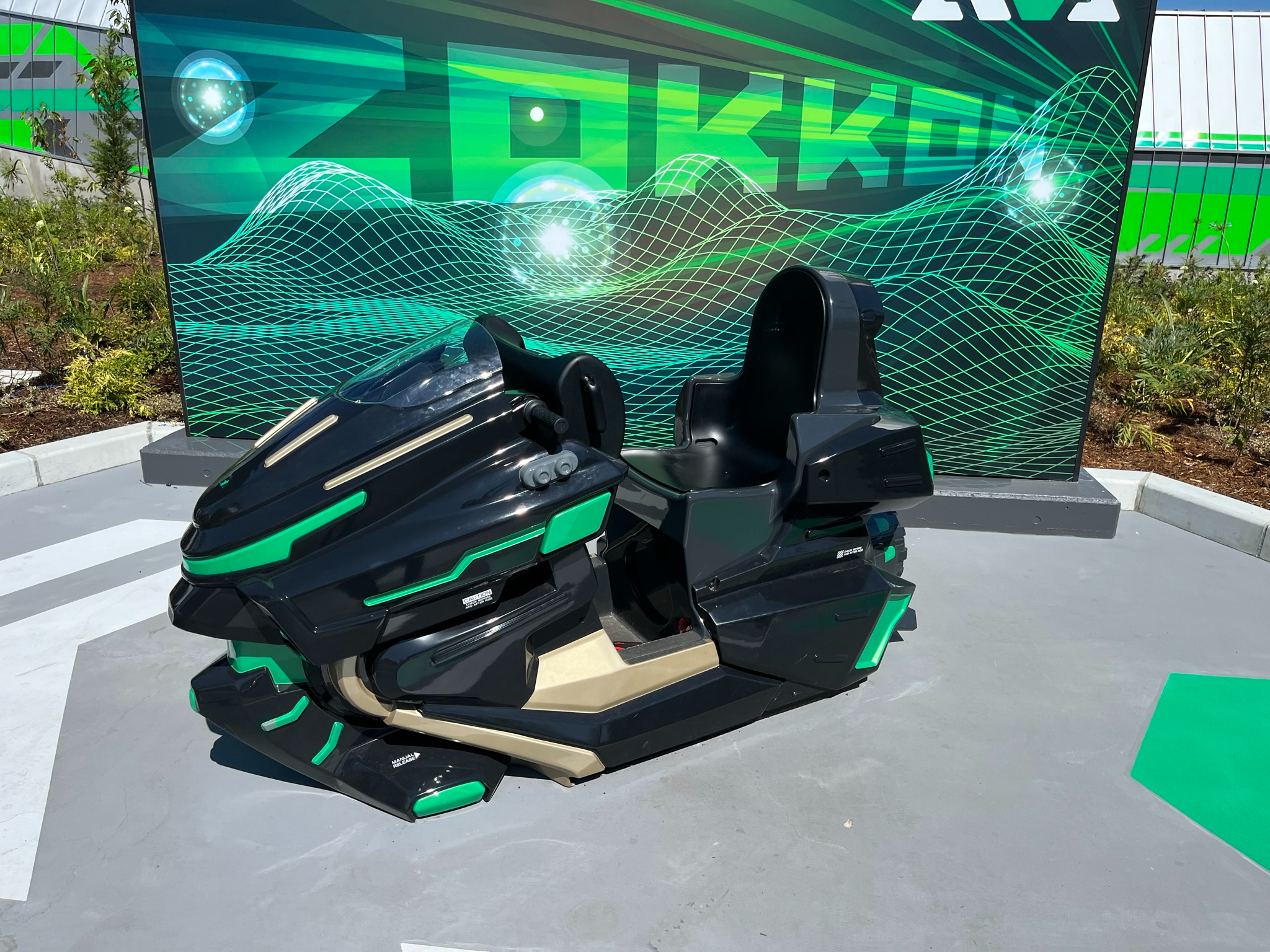Motorcycle-style ride vehicle for Fuji-Q Highland's ZOKKON coaster, displayed in front of a green futuristic backdrop featuring the attraction's name and digital graphics.