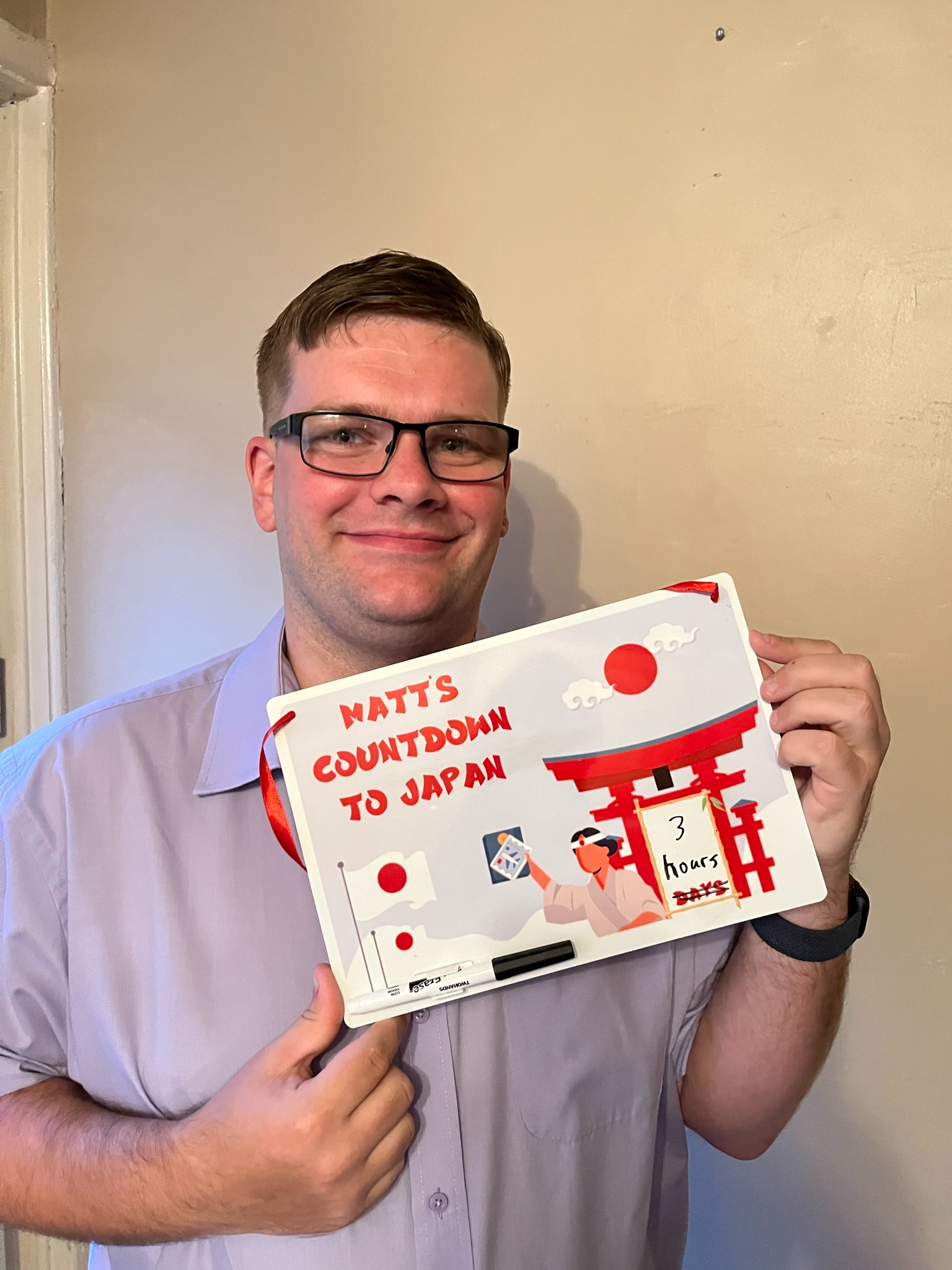 Person holding a custom "Countdown to Japan" whiteboard featuring a torii gate and Japanese-themed graphics, showing just three hours remaining before departure.