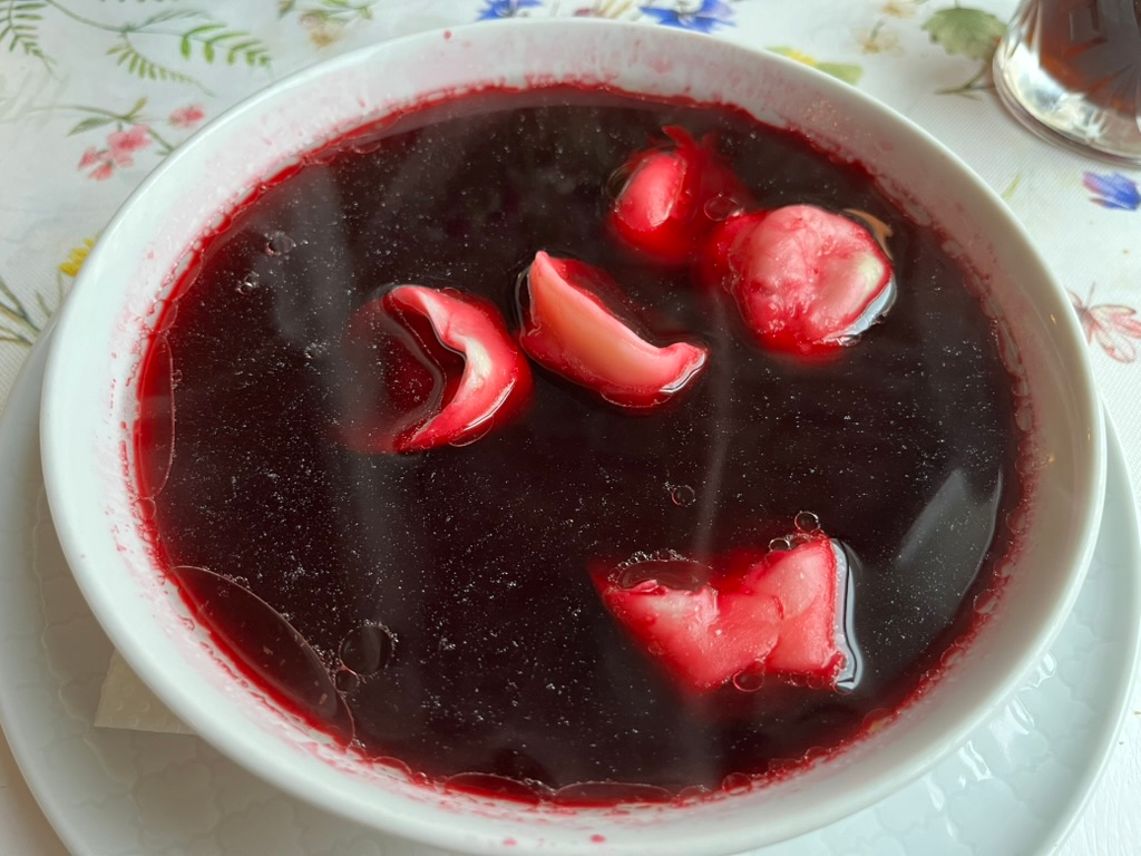 Bowl of deep red borscht served with small dumplings floating on the surface.