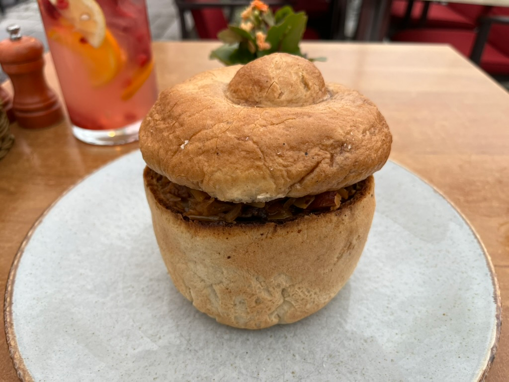 Traditional Polish bigos served in a hollowed bread bowl with a bread lid, presented on a ceramic plate.