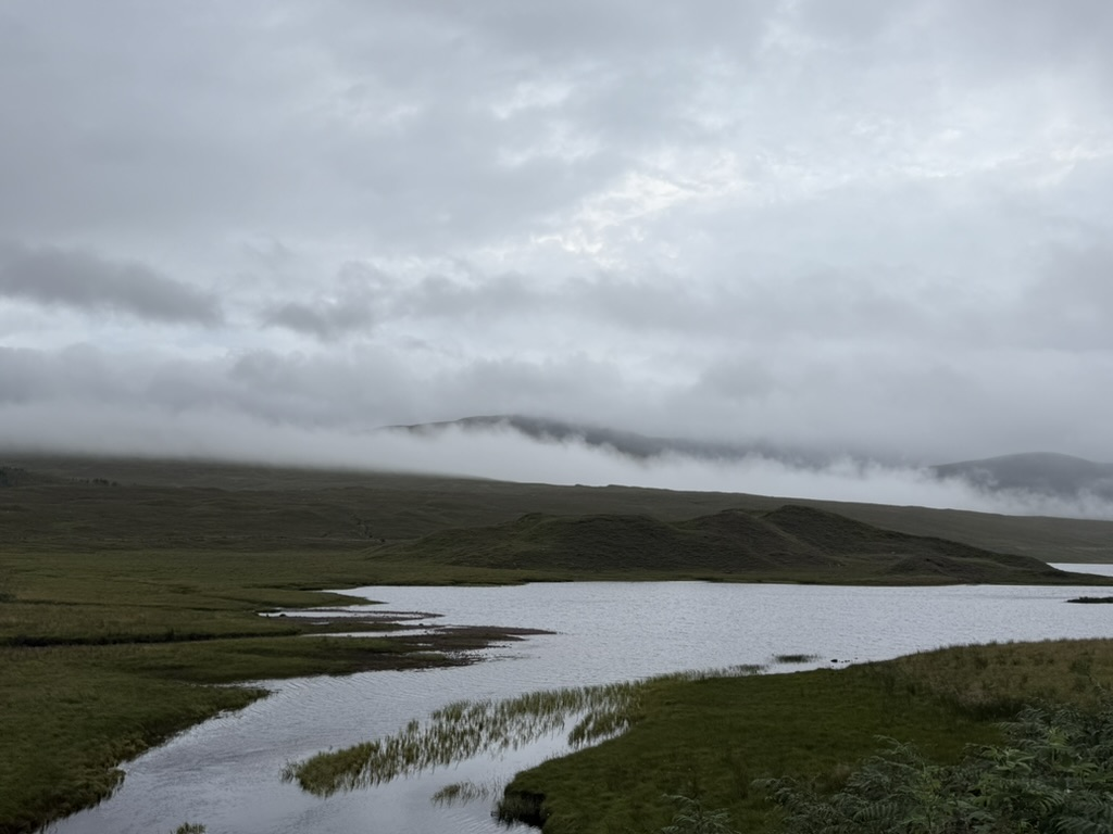 Misty Highland loch surrounded by rolling hills beneath low cloud.