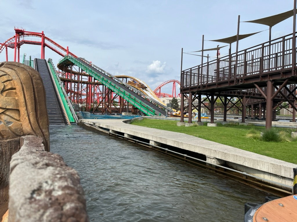 Anaconda water coaster at Energylandia, with boats climbing a lift hill above a water channel, surrounded by themed structures and roller coaster track in the background.