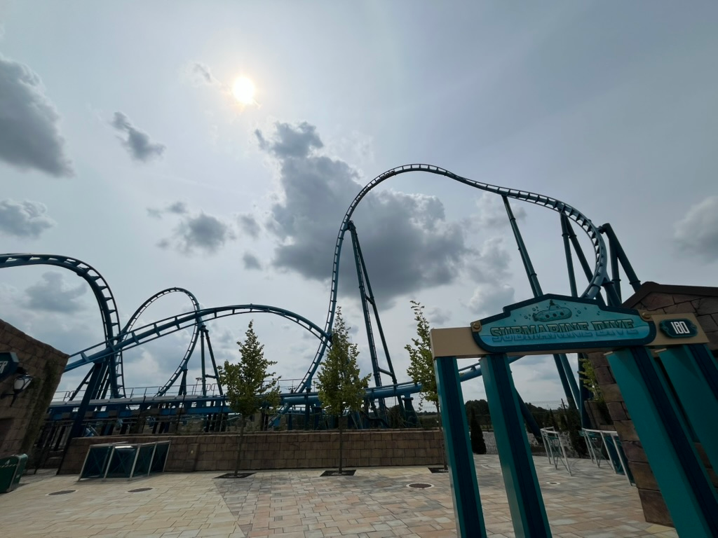 Abyssus roller coaster at Energylandia, featuring blue track and sweeping inversions above a themed plaza under a cloudy sky.