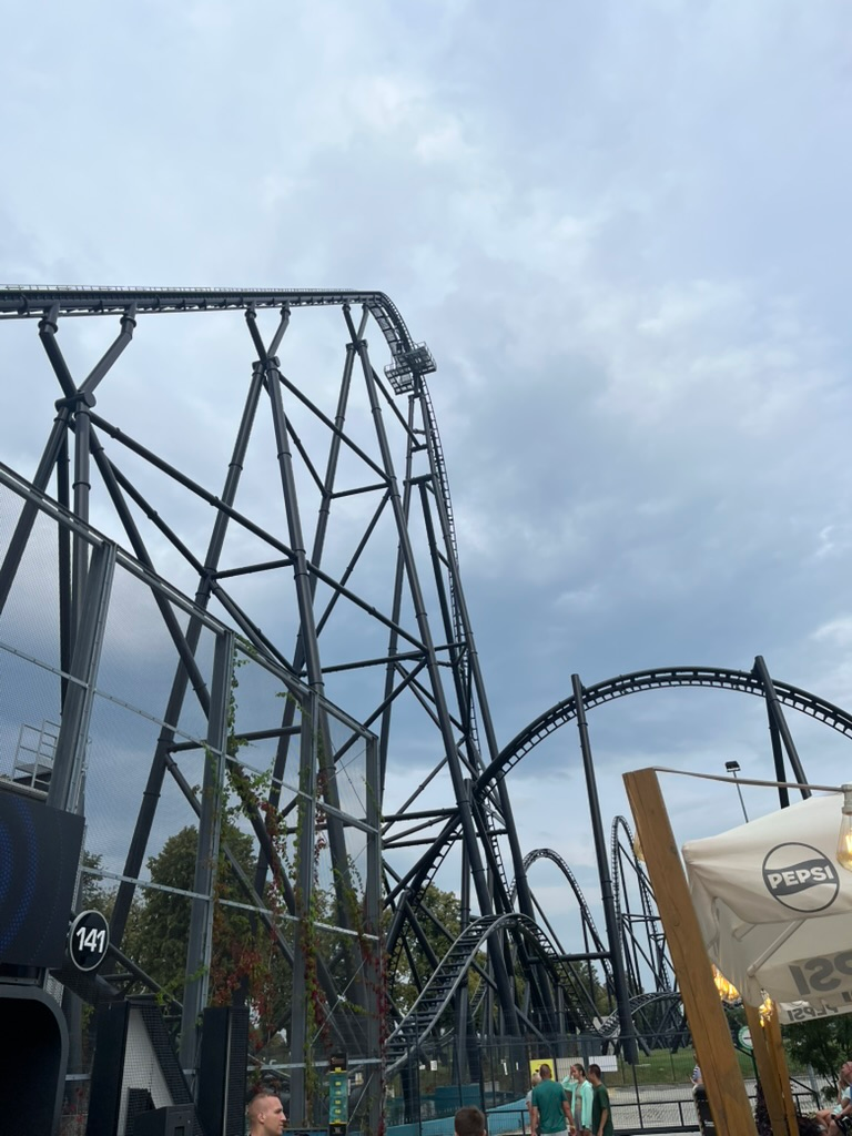 Hyperion roller coaster at Energylandia, featuring its towering black steel drop and twisting track sections beneath a cloudy evening sky.