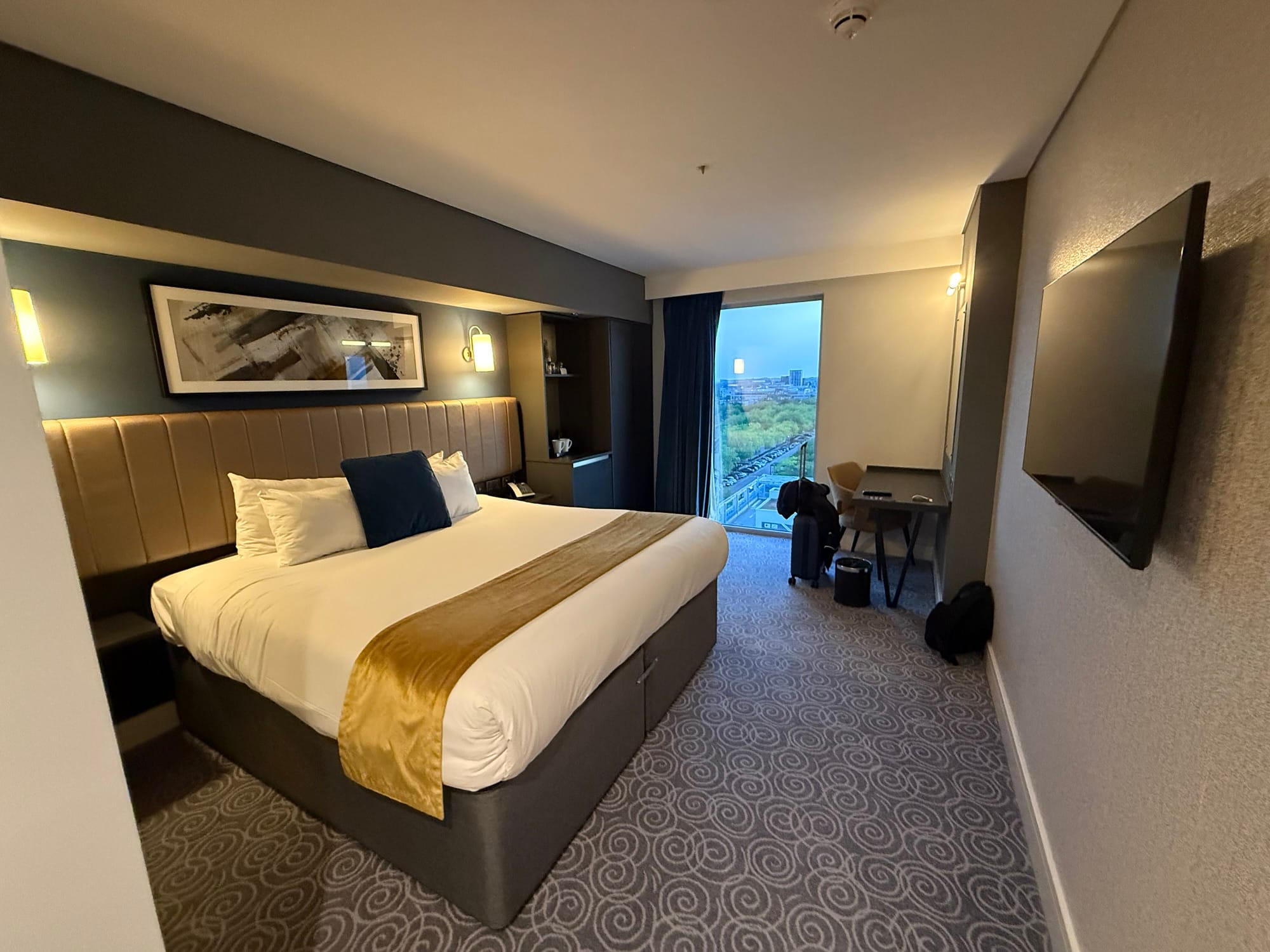 Modern hotel room with king-size bed, desk and city view.