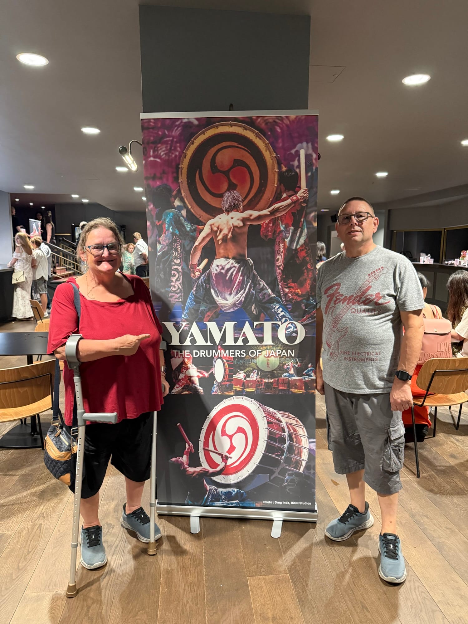 Two people standing beside a Yamato Drummers of Japan promotional banner at the Peacock Theatre in London.