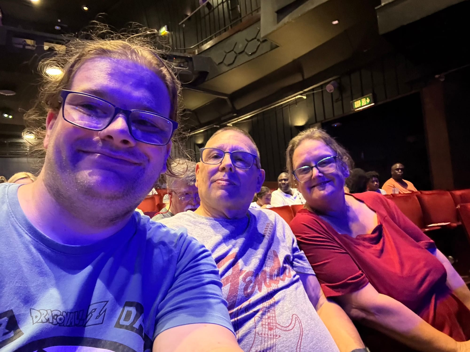Three people seated inside the Peacock Theatre in London before a performance.