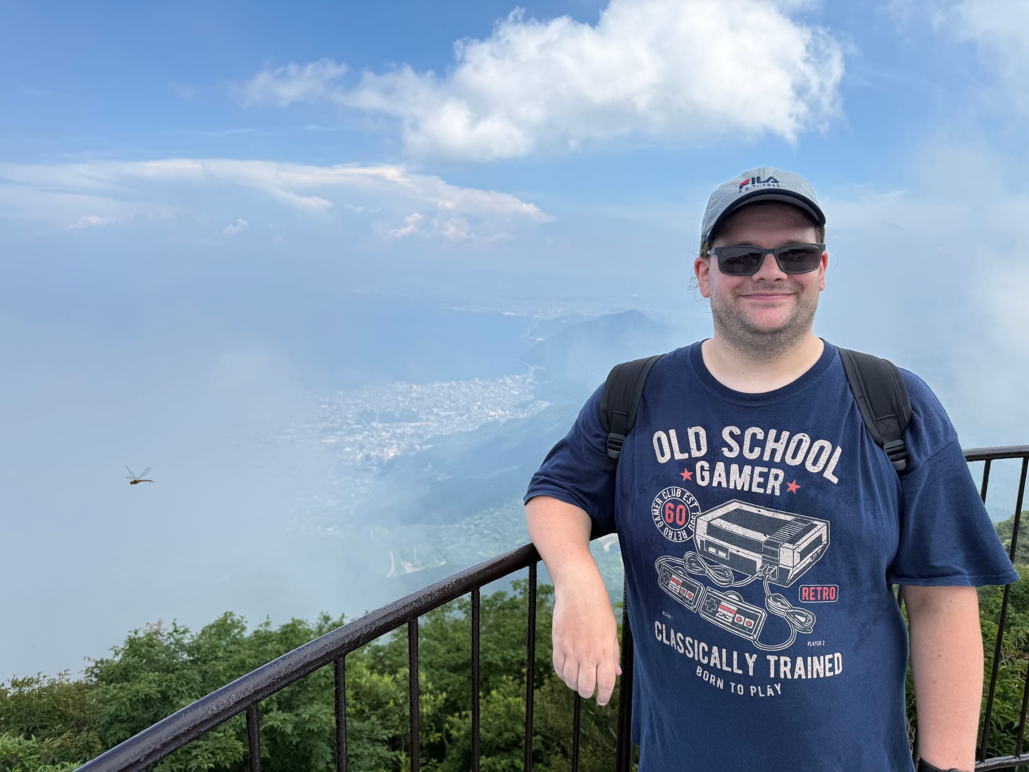 Visitor stands at a viewpoint on Mount Tsurumi above Beppu, with clouds drifting across the landscape and Beppu Bay faintly visible below in the distance.