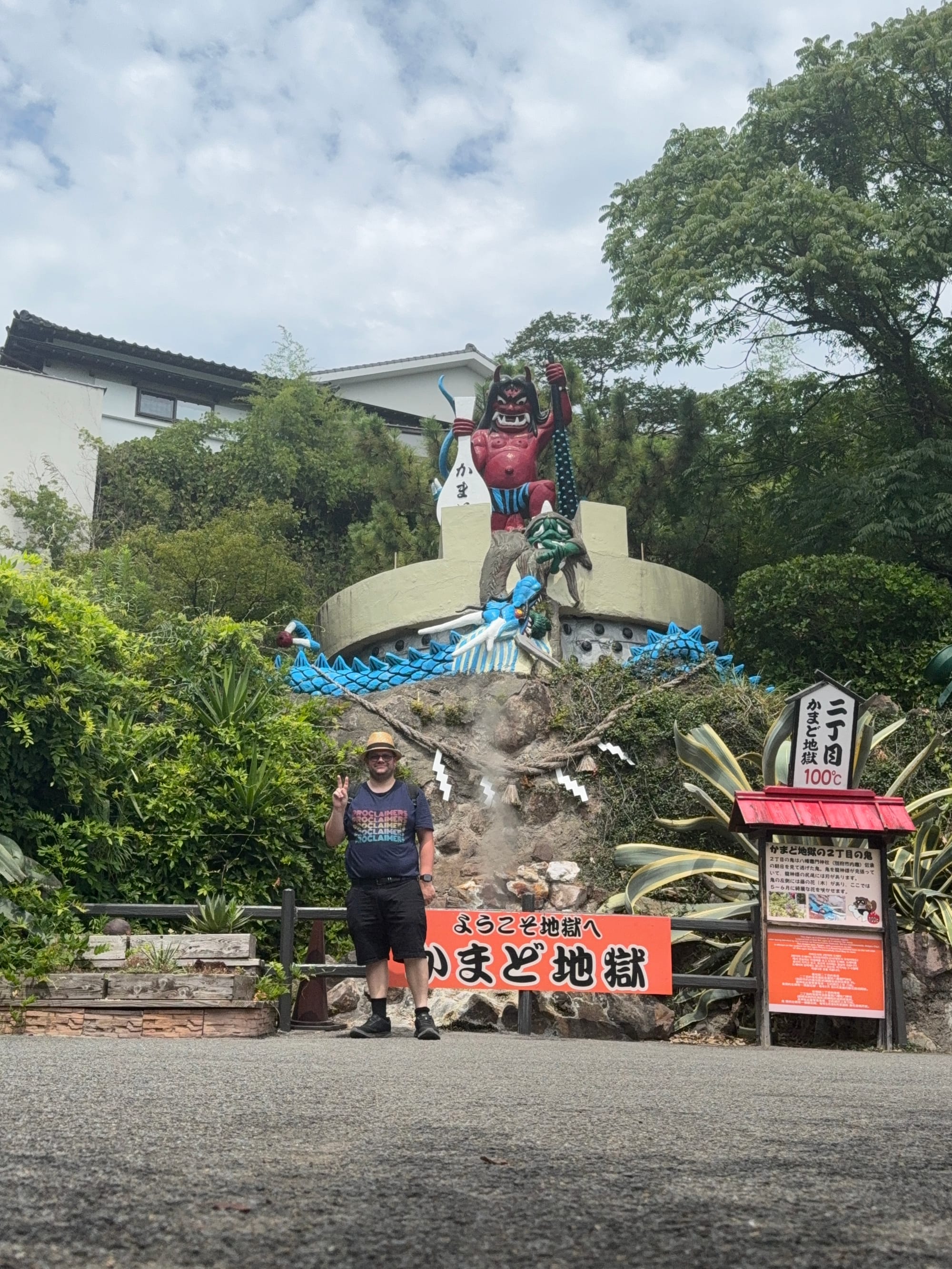 Visitor posing at Kamado Jigoku in Beppu, making a peace sign beneath a large red oni statue and dragon-themed display marking one of the city's famous hot spring hells.