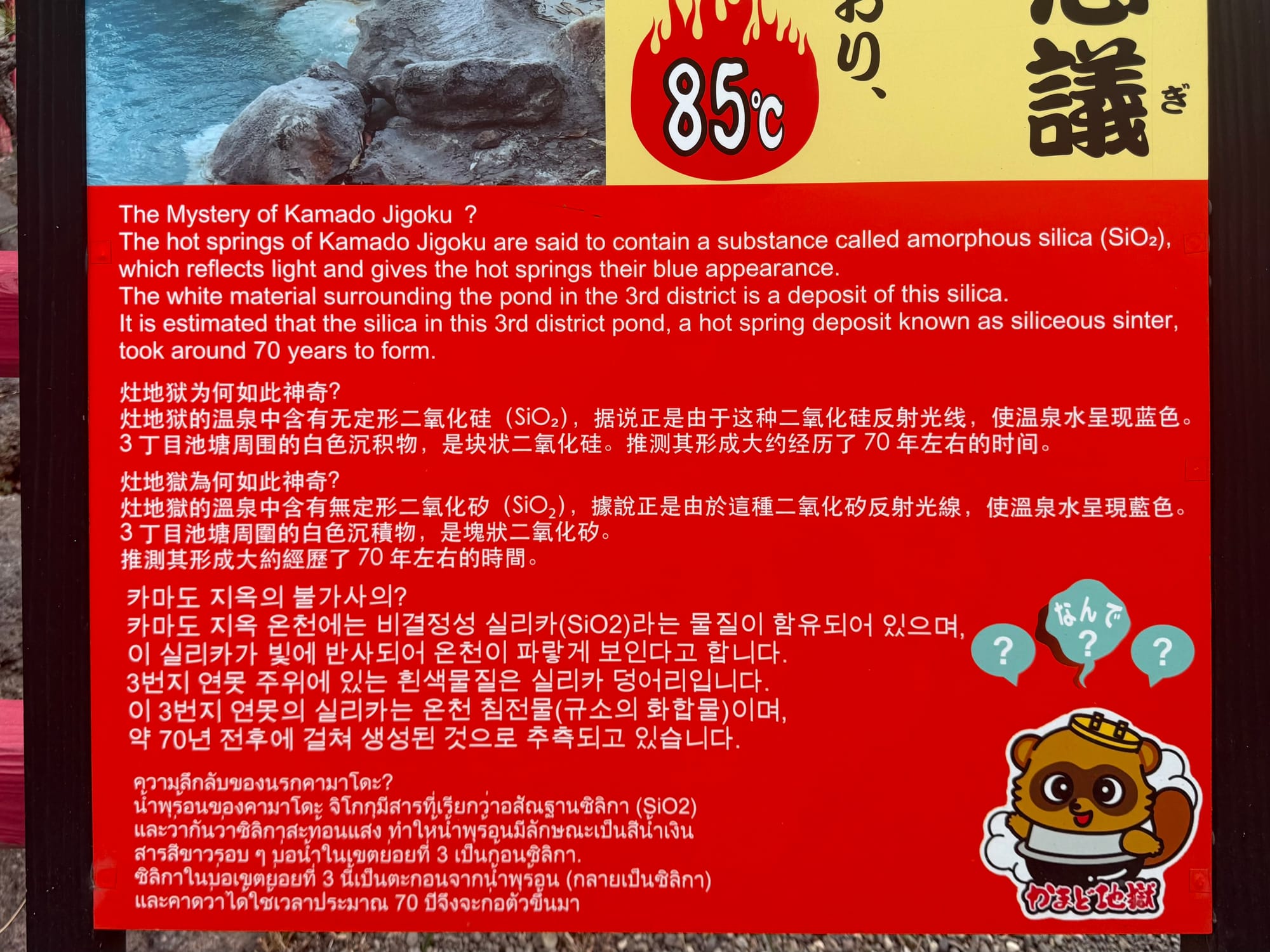 Information board at Kamado Jigoku explaining the blue colour of an 85°C geothermal pond, caused by silica in the hot spring water and surrounding mineral deposits.