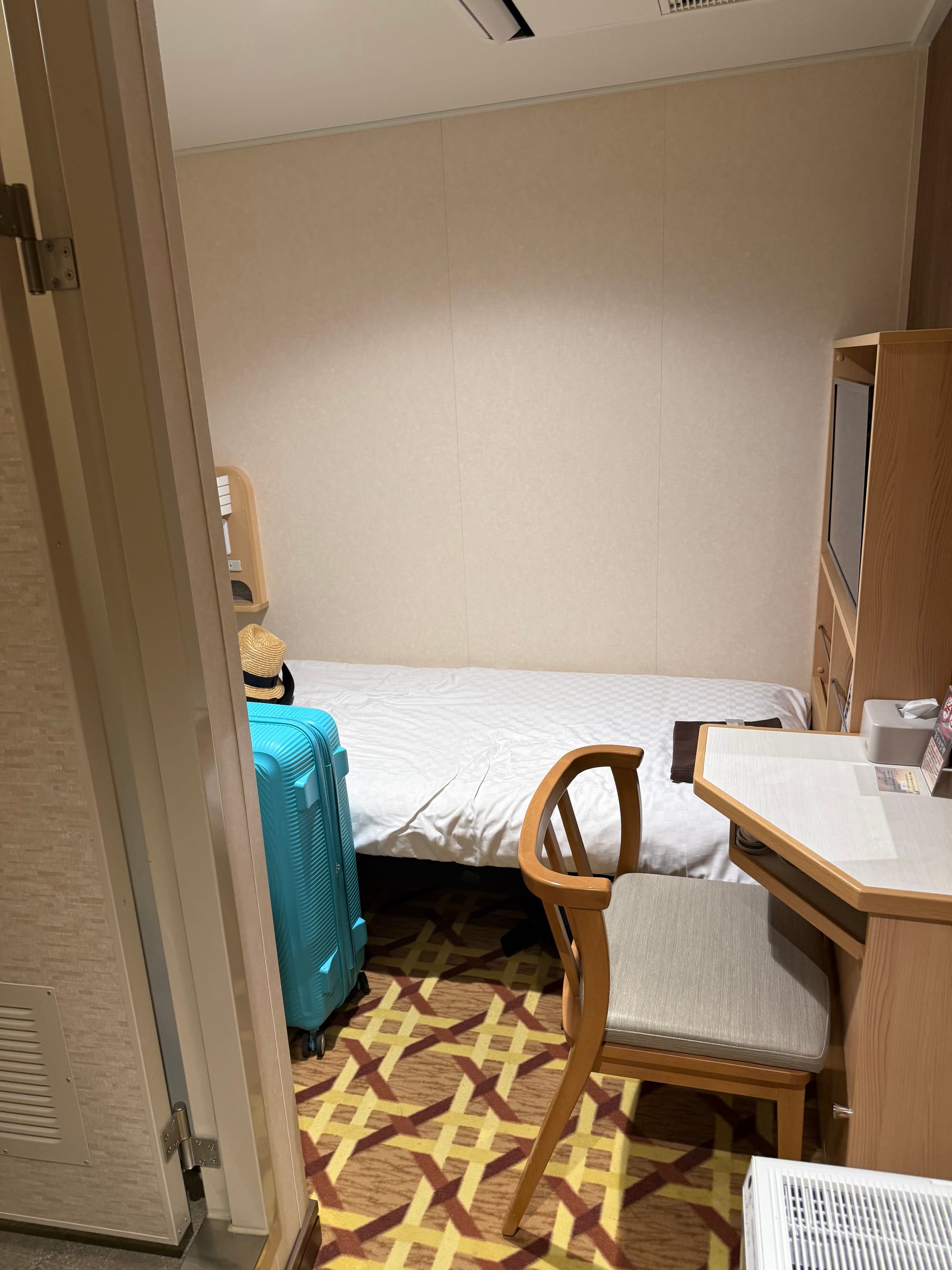 Compact private cabin aboard the Sunflower Ferry, featuring a single bed, desk, chair, television, storage unit, air conditioning and luggage in a space-efficient layout.