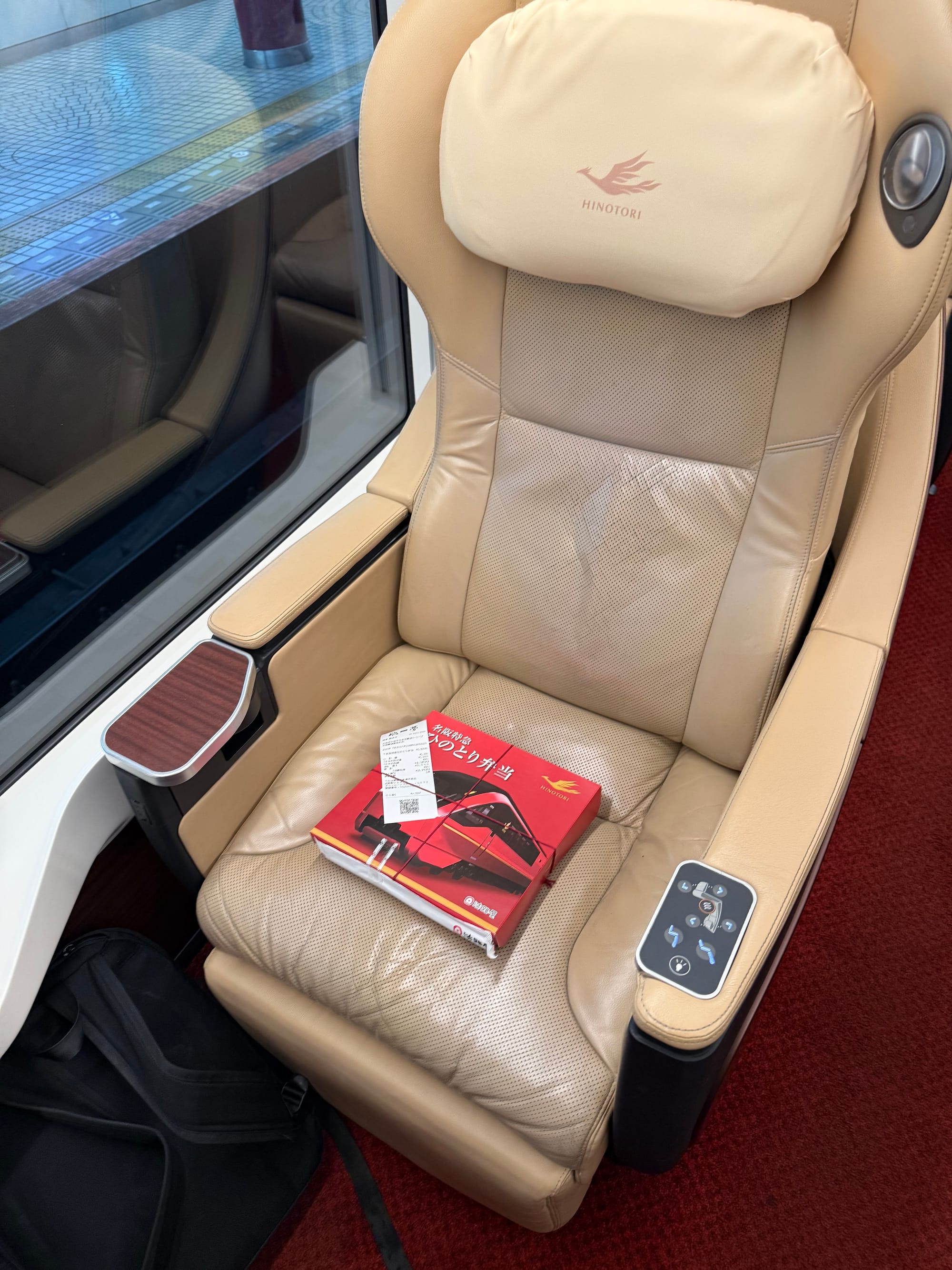 Premium reclining seat aboard a Kintetsu Hinotori limited express train, with adjustable controls, a window-side table and a Hinotori ekiben placed on the seat.