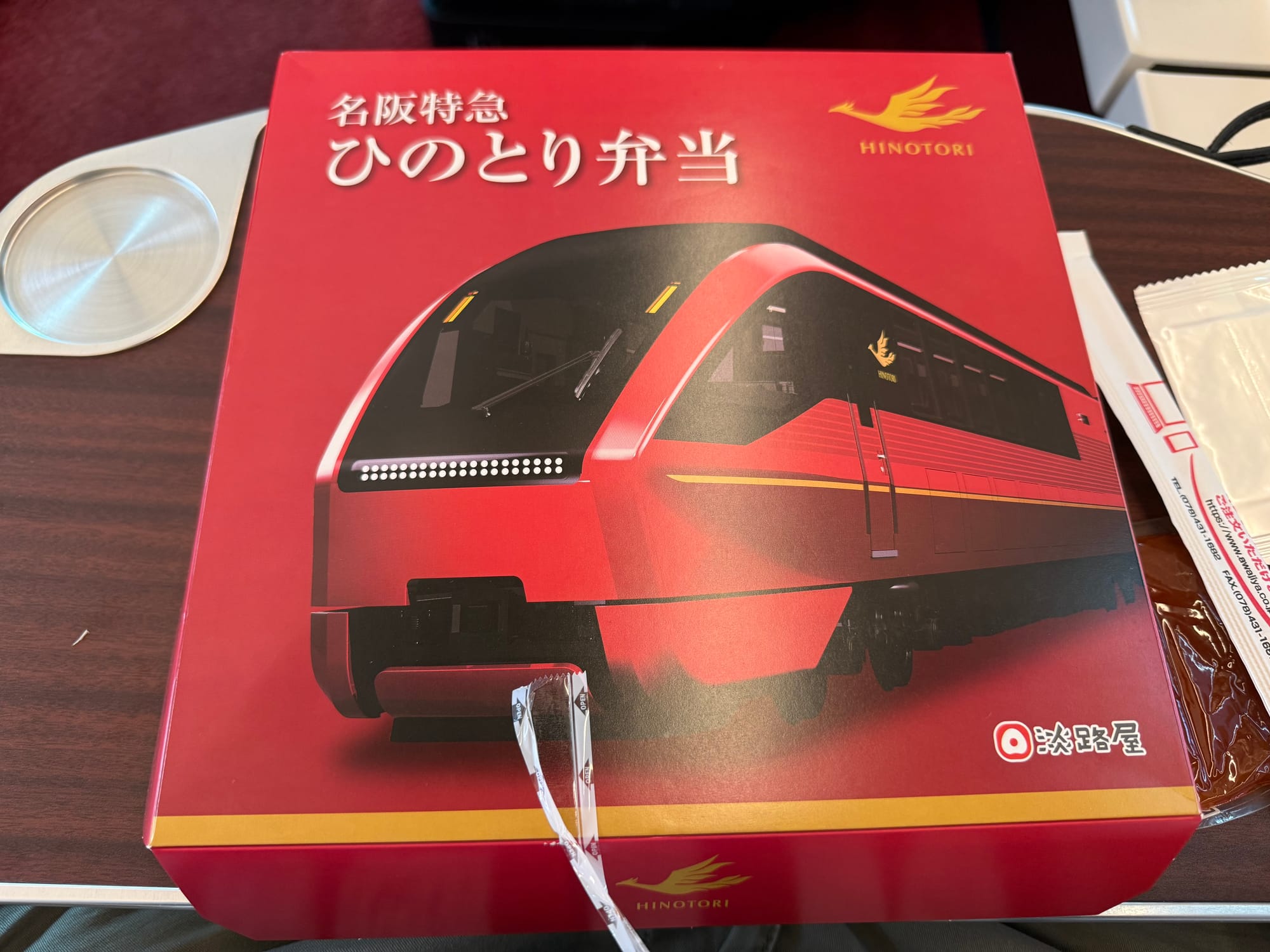 Hinotori-themed ekiben box on a table aboard the Kintetsu Hinotori limited express, featuring artwork of the train in its distinctive deep red livery.