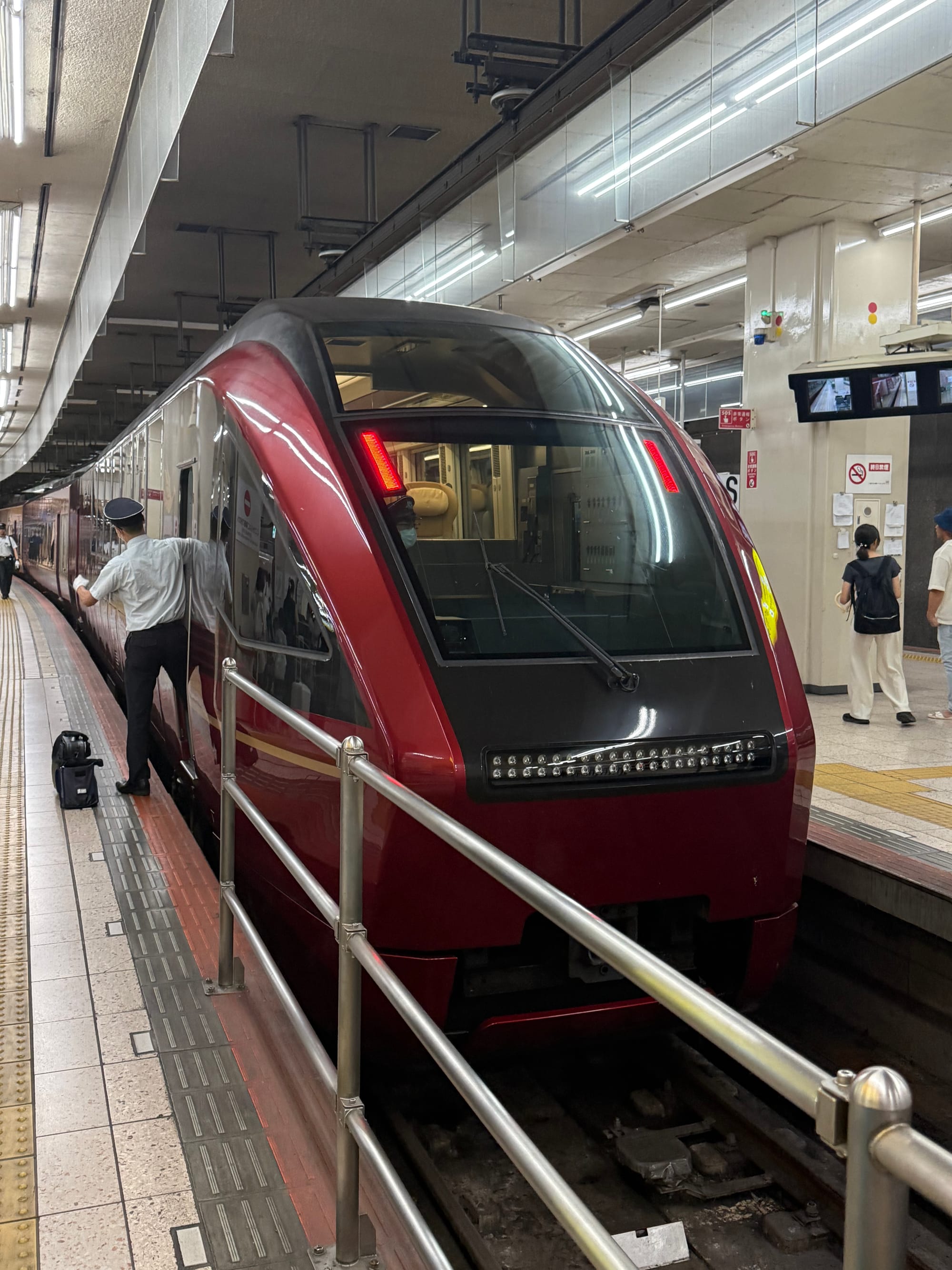 Kintetsu Hinotori limited express train standing at a station platform, showing its distinctive deep red livery, panoramic rear window and sleek modern design.