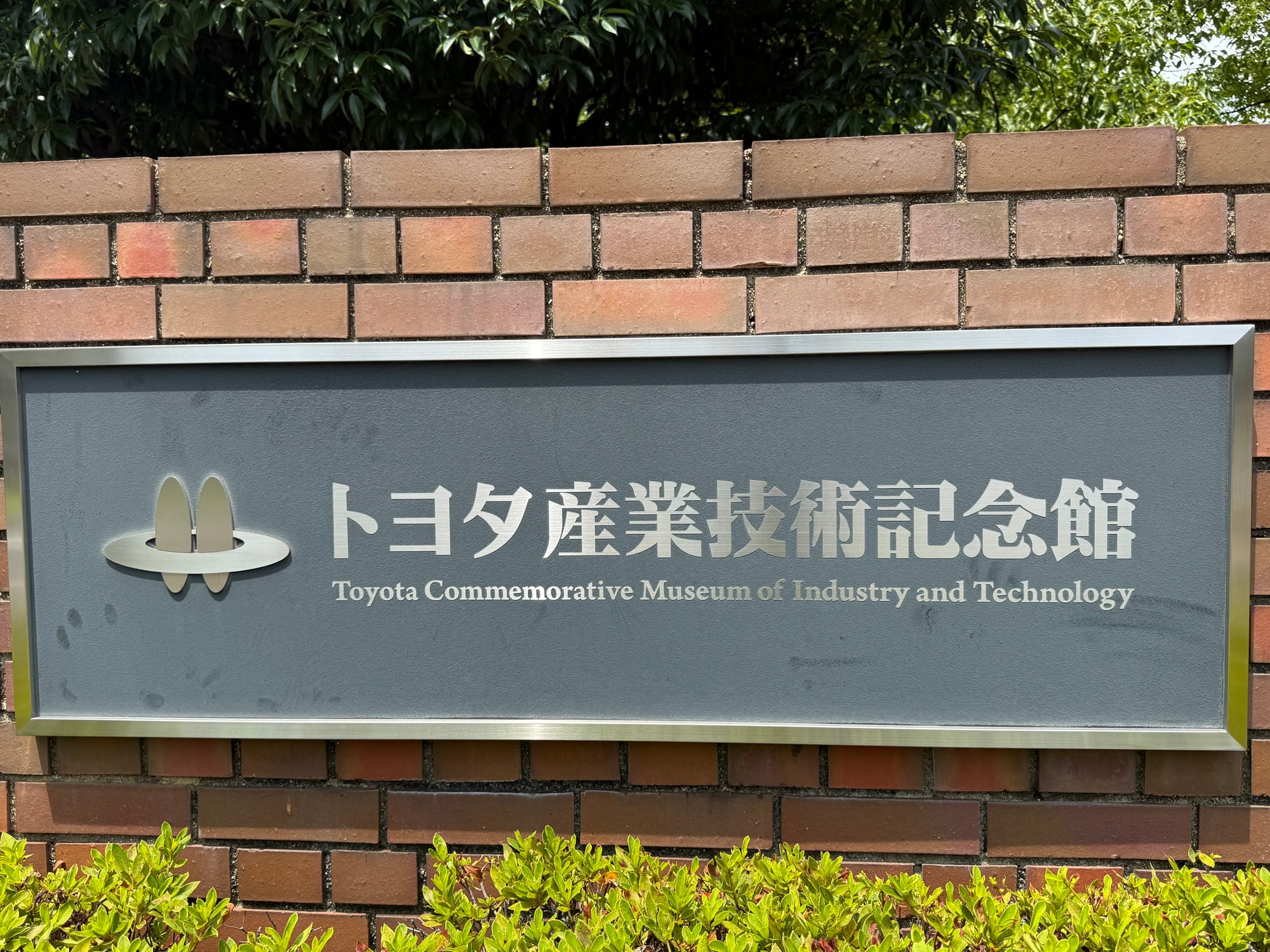Sign for the Toyota Commemorative Museum of Industry and Technology in Nagoya, mounted on a brick wall with Japanese and English text beside the museum logo.