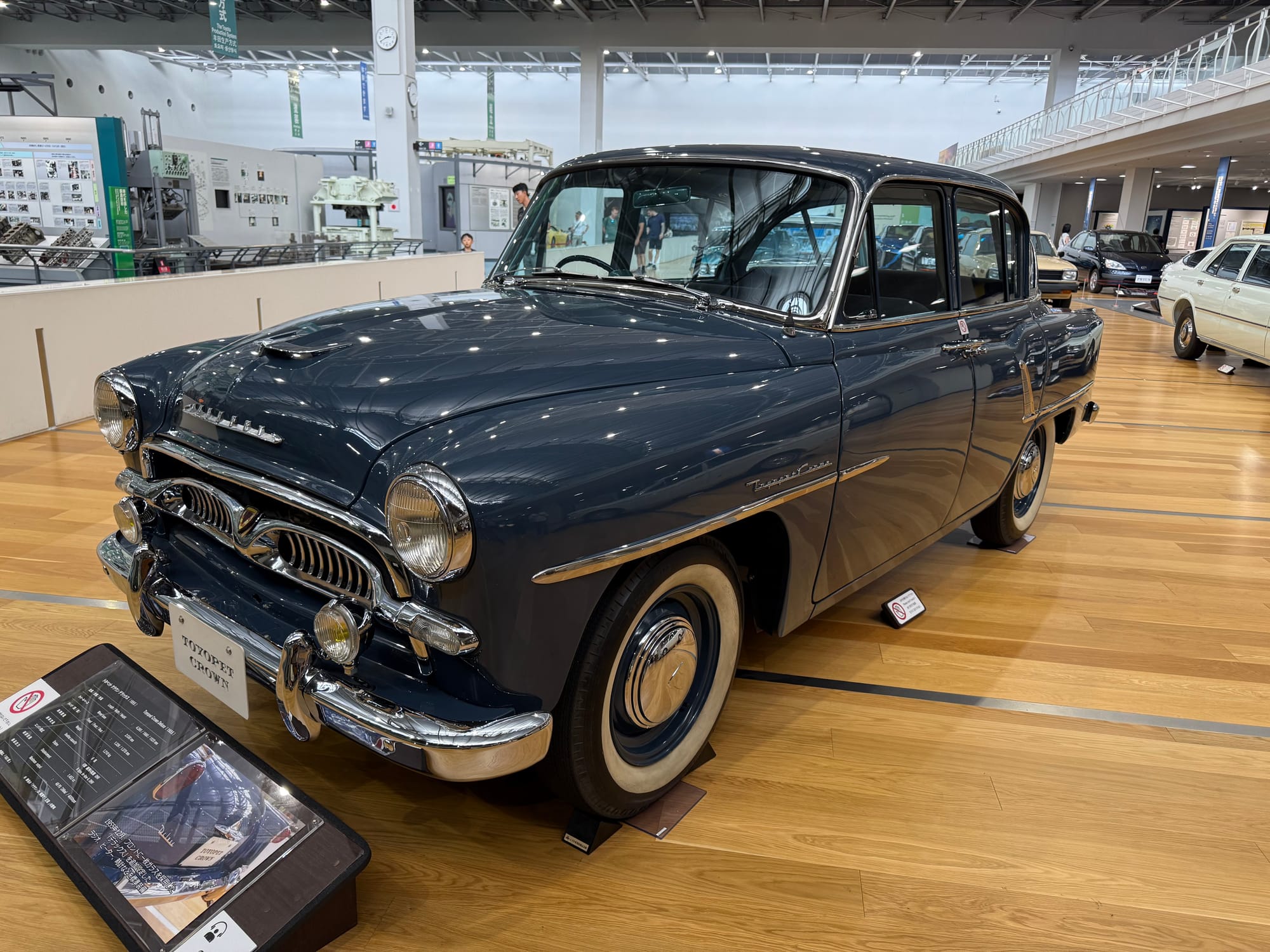 Toyota Crown sedan on display at the Toyota Commemorative Museum of Industry and Technology, featuring dark blue bodywork, chrome detailing and distinctive 1950s styling.