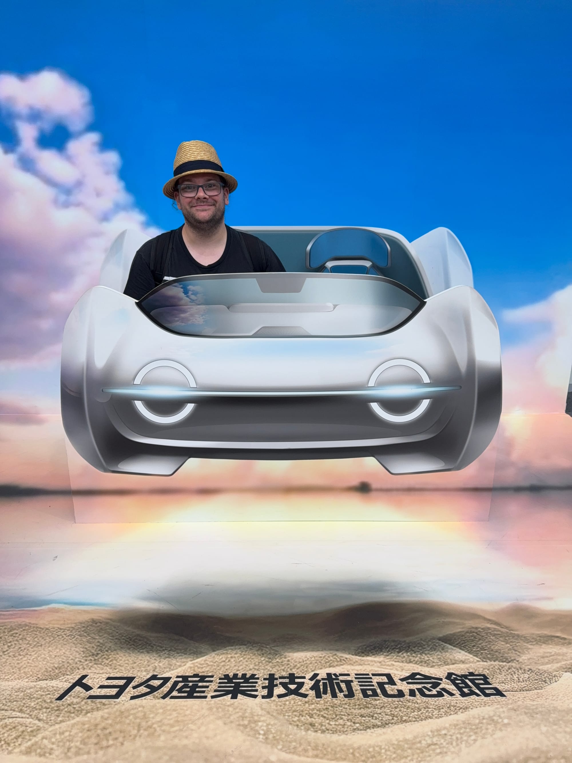 Visitor posing behind a futuristic concept car display at the Toyota Commemorative Museum of Industry and Technology, creating the illusion of sitting inside a futuristic vehicle.