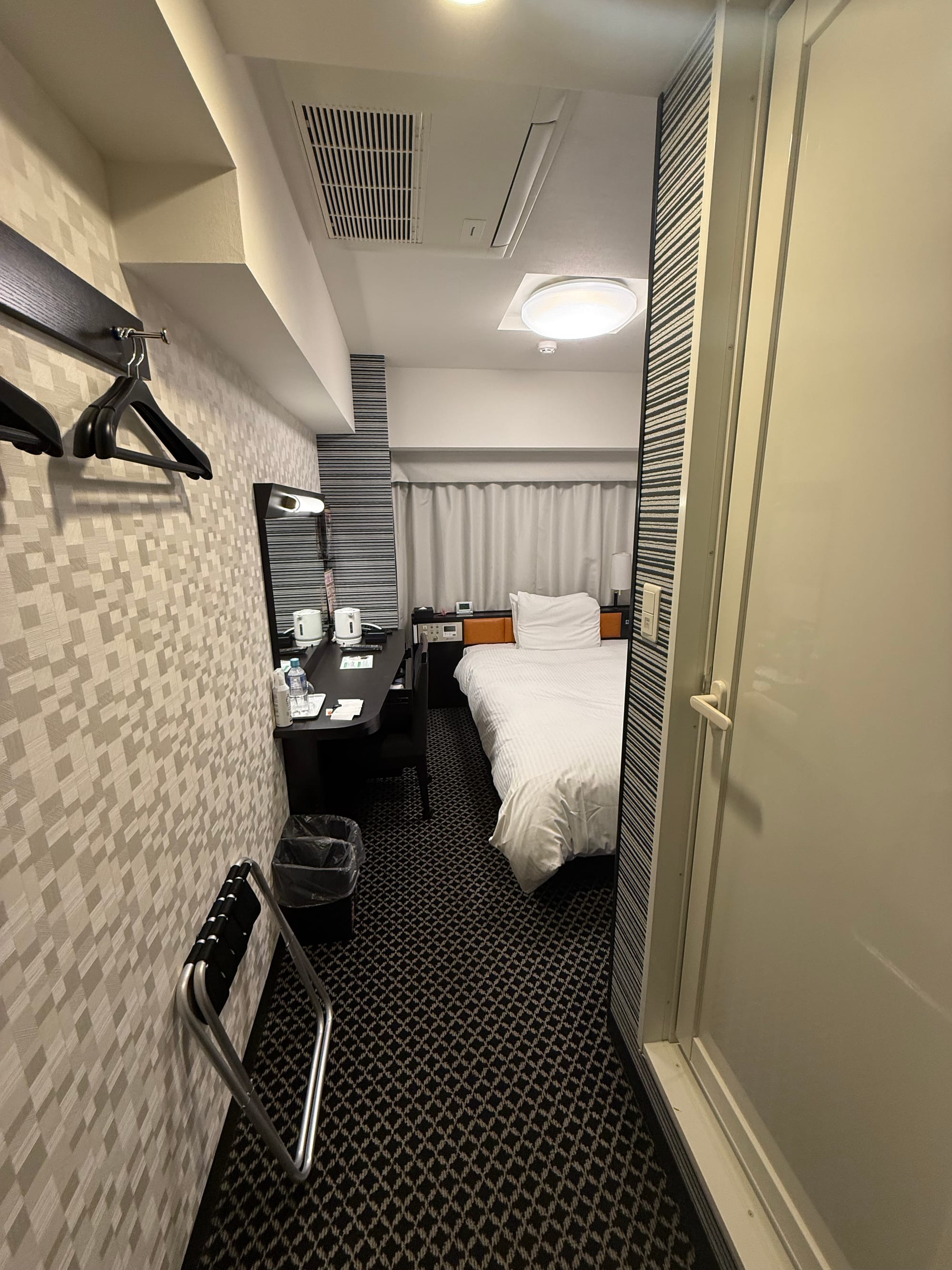 Compact single room at APA Hotel Nagoya Sakae-Kita, featuring a bed, desk, kettle, luggage rack and en-suite bathroom arranged in a space-efficient layout.