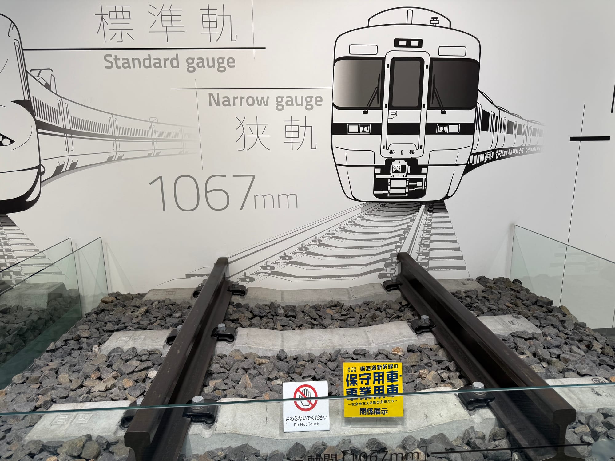 Narrow-gauge railway track display at the SCMAGLEV and Railway Park, showing Japan's 1,067 mm gauge alongside an illustration of a conventional limited express train.